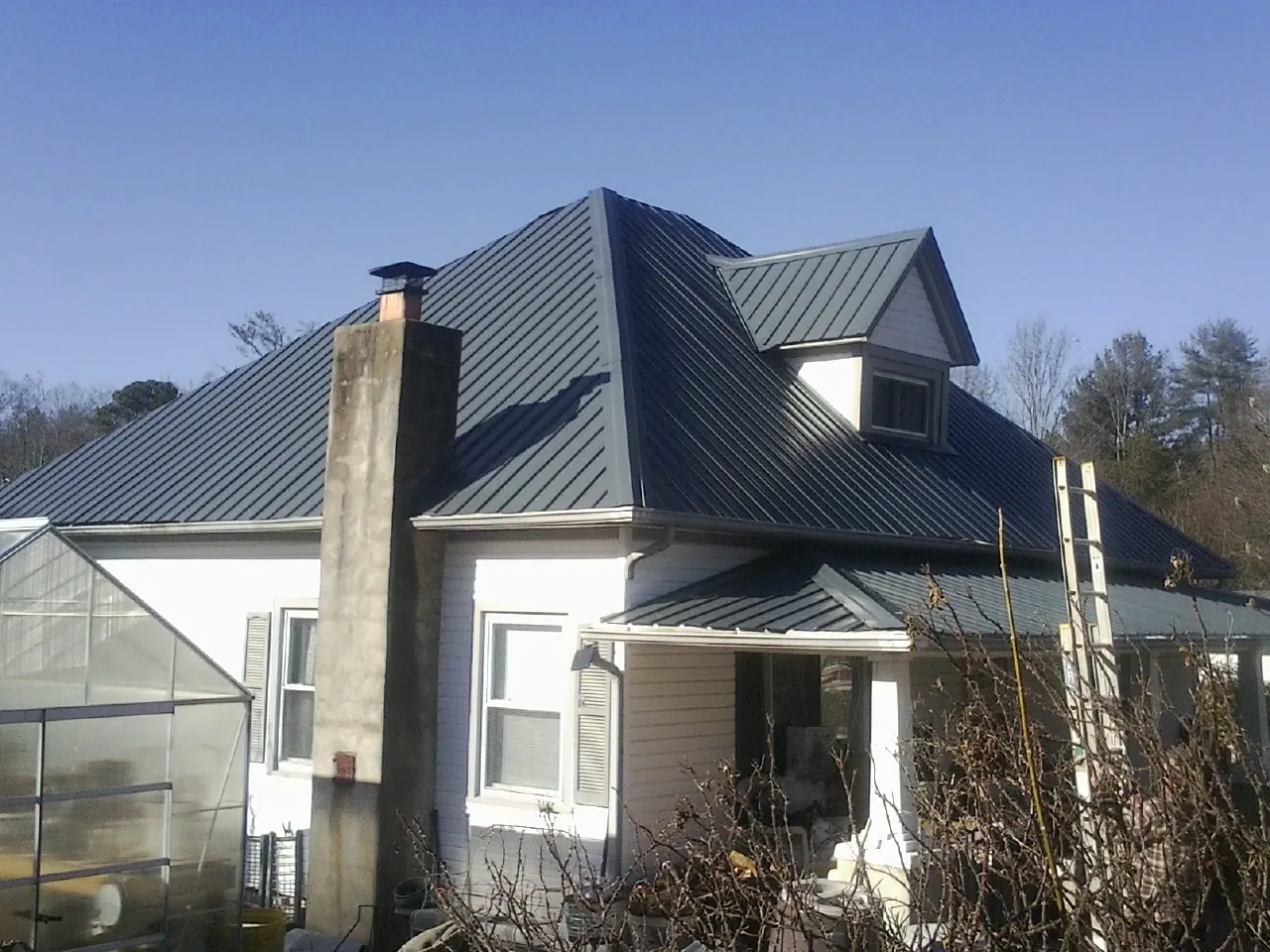 Dark blue standing seam metal roof on a white farmhouse with dormer — Slate & Tile Roof Repair by Roofing Brothers in Fossil