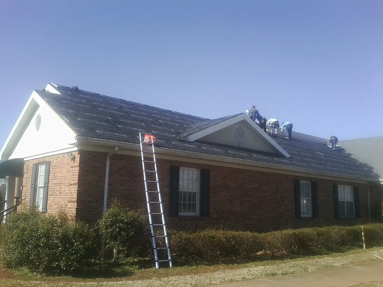 Crew tearing shingles off a brick ranch roof with a ladder set — Metal Roof Repair work by our crew in Fossil