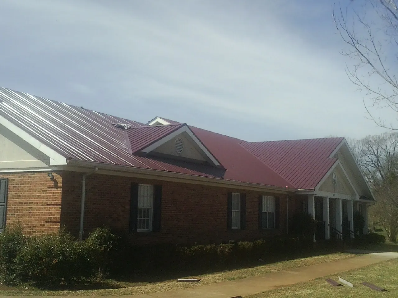 Red metal roof with gabled entries on a long brick building, from a Hail Damage Roof Repair job in Fossil