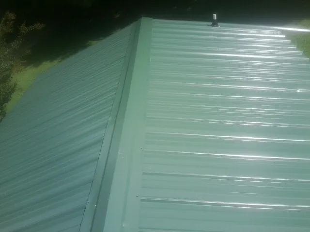 New green metal panels meeting at the ridge of a roof — Flat Roof Repair work by our crew in Fossil