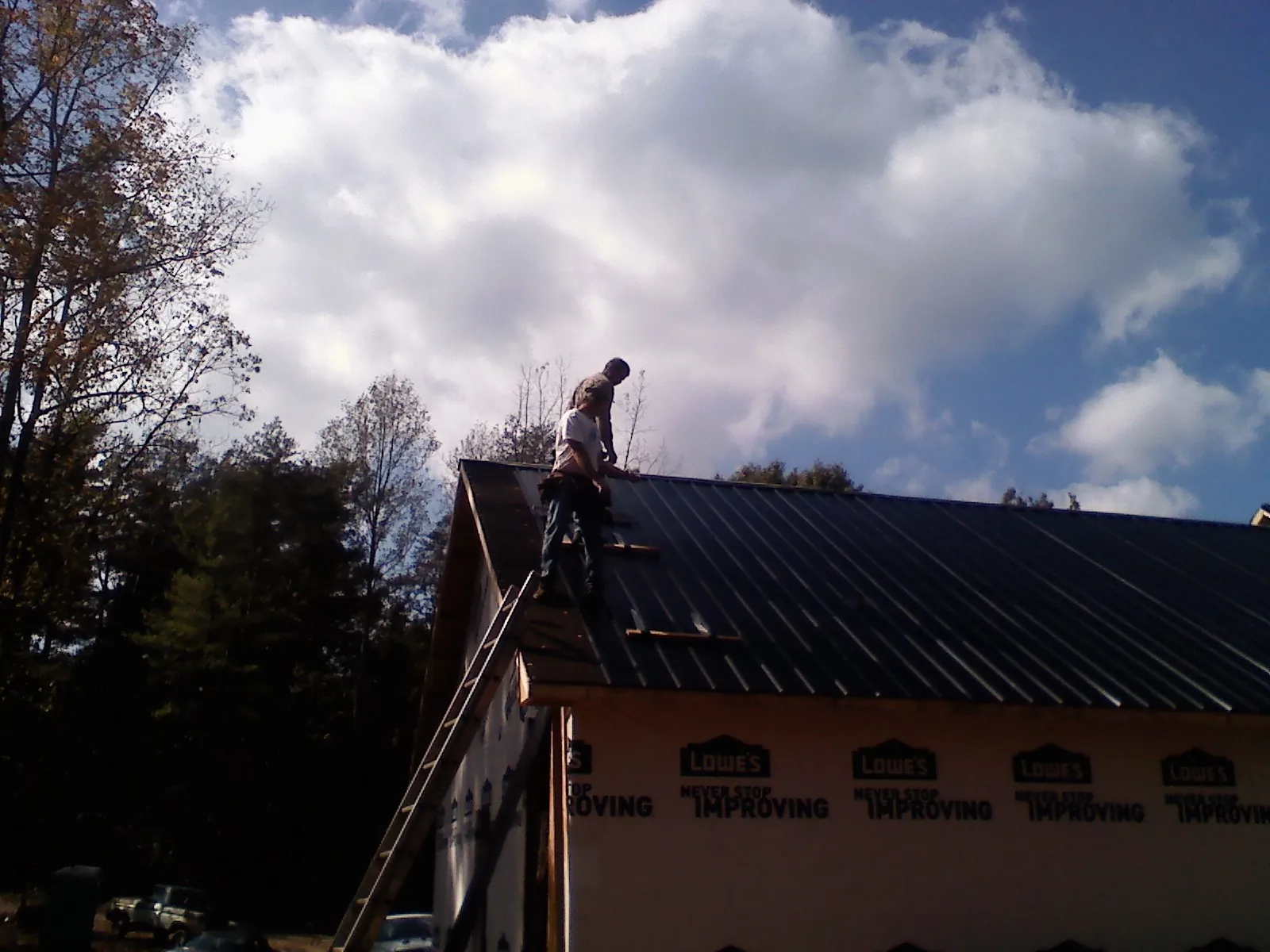 Roofer fastening dark metal panels high against a cloudy sky, from a Roof Inspection job in Fossil